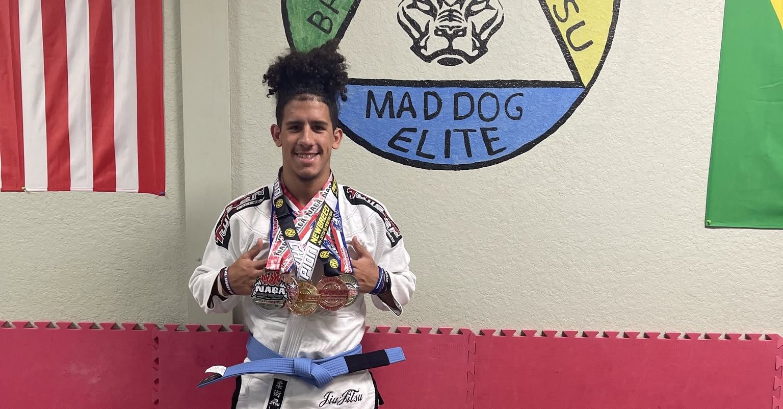 A Mad Dog Elite student wearing a stack of tournament medals beneath the academy's wall logo